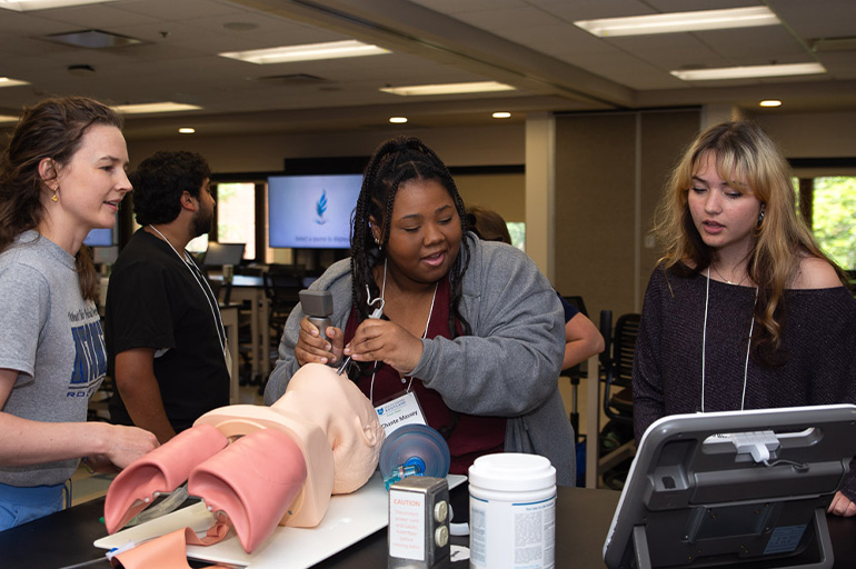 Three young women practice intubation with a medical simulation manikin