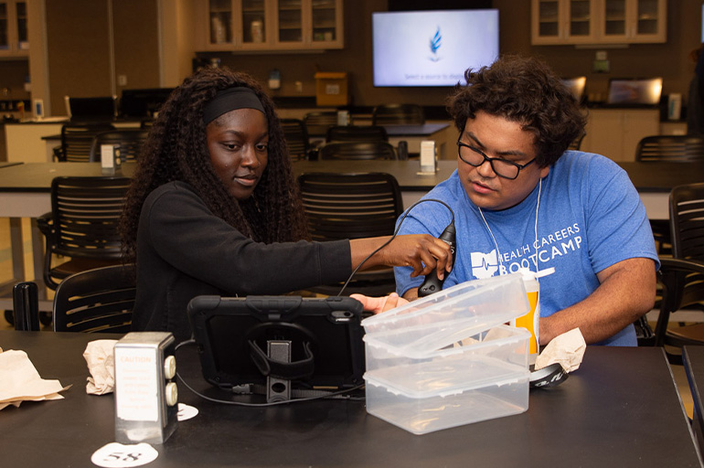 A young woman in a black shirt practices with an ultrasound device with an observer in a blue T-shirt