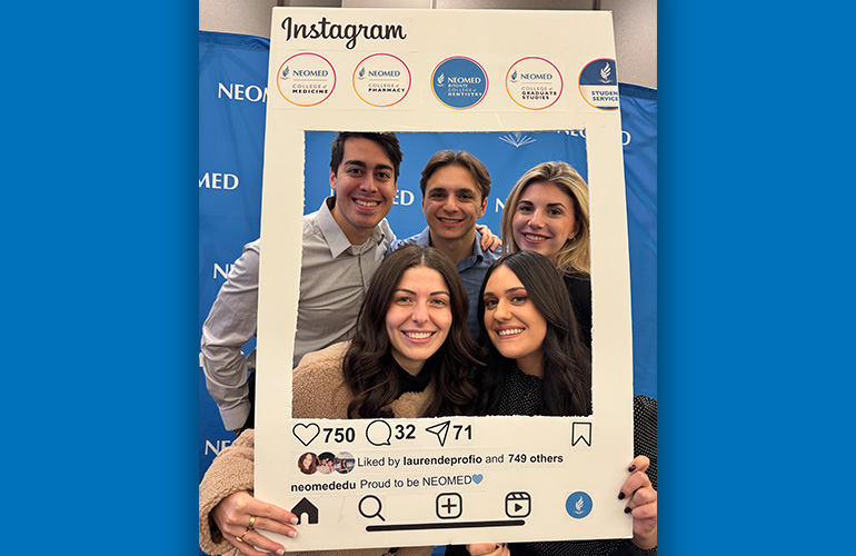 a group of three women and two men pose in a cut out frame mimicking an Instragram post