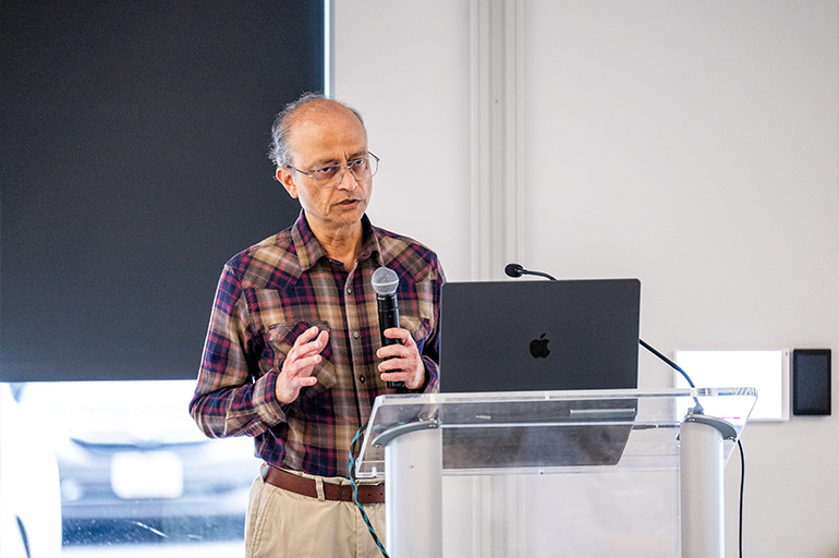 a man in a brown plaid shirt speaks at a modern podium