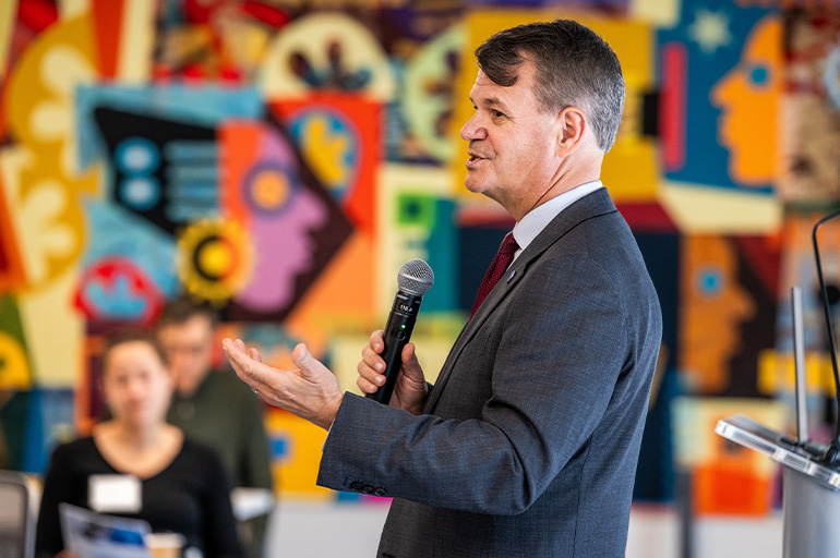 NEOMED President John Langell speaks. a colorful mural is on the wall in the background
