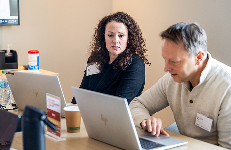 A woman and man in business casual attire work side by side on laptops