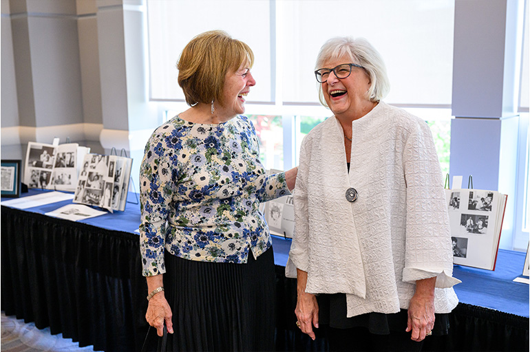 two women chat happily while standing in front of a display of old photos and yearbooks