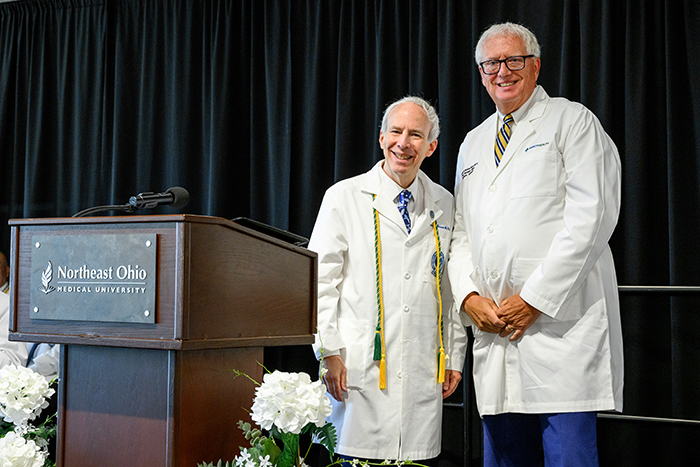 Two men in white coats stand next to a podium adorned with the NEOMED logo