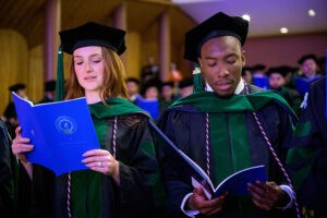 A woman and a man in the academic regalia of the NEOMED College of Medicine recite an oath from the program at commencement