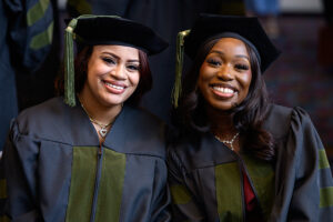 Two young women dressed in academic regalia at commencement to receive their Pharm.D. degrees
