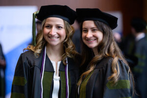 two young women in academic regalia smile at something off camera