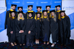 A group of graduating students in academic regalia pose in front of NEOMED-branded backdrops