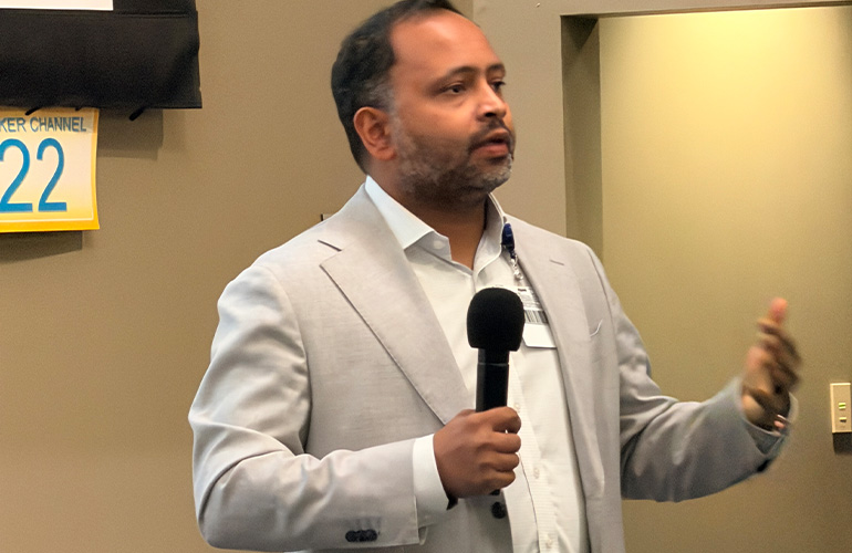 Man in tan suit speaks into a microphone