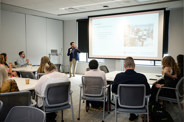 A man stands in front of a classroom explaining a slide display to an audience