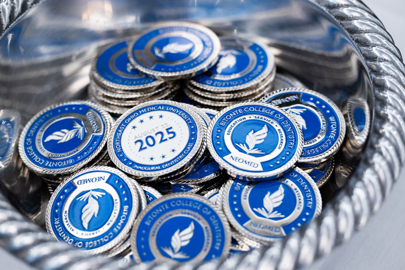 A silver tray holding blue and white challenge coins with the college's logo on them.
