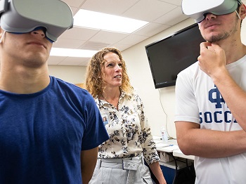 A woman stands between two men, each wearing a virtual reality headset.