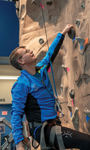 President Langell scales the climbing wall at the on-campus wellness center.