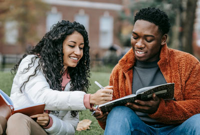 Two college students studying together outdoors, enjoying collaborative learning.