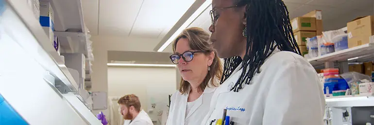 Two women in lab coats at work in a NEOMED research lab.