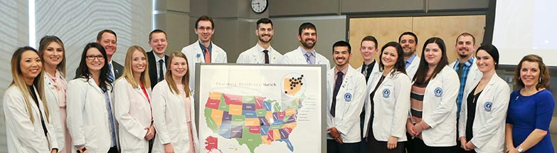 Pharmacy students gather around a map of the United States showing where graduates are employed.