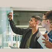 Two students at a whiteboard work together to solve a problem.