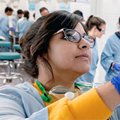 A medical student in blue scrubs works in a lab.