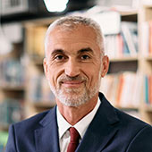 A faculty member in a coat and tie with books in the background.