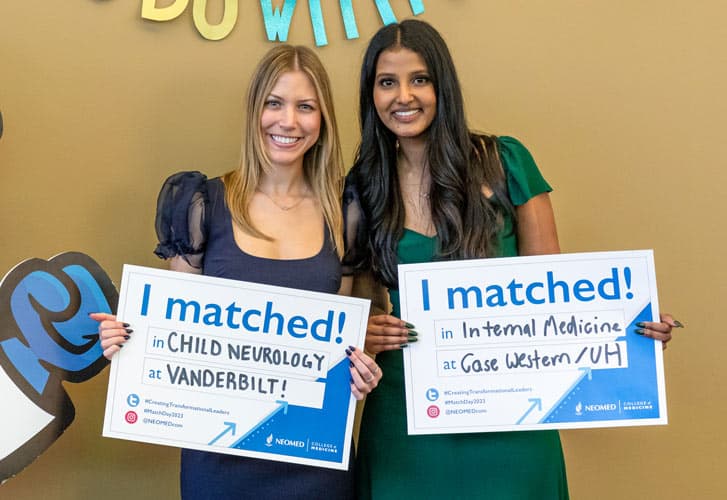 Two medical students hold signs with where they will complete their residencies.