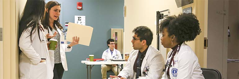 Medical students and doctors confer in a hallway.