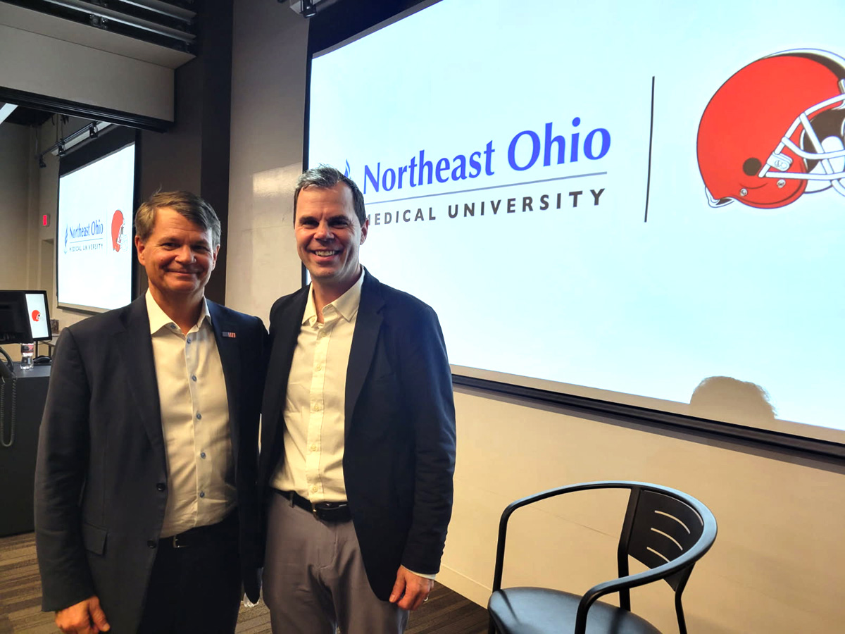 Two men smiling and standing in front of projected presentation with co-branded logo