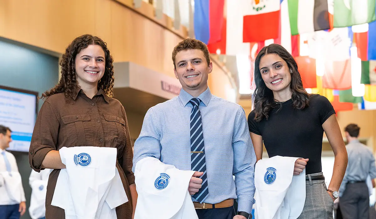 Three NEOMED students hold their white coats before a ceremony.