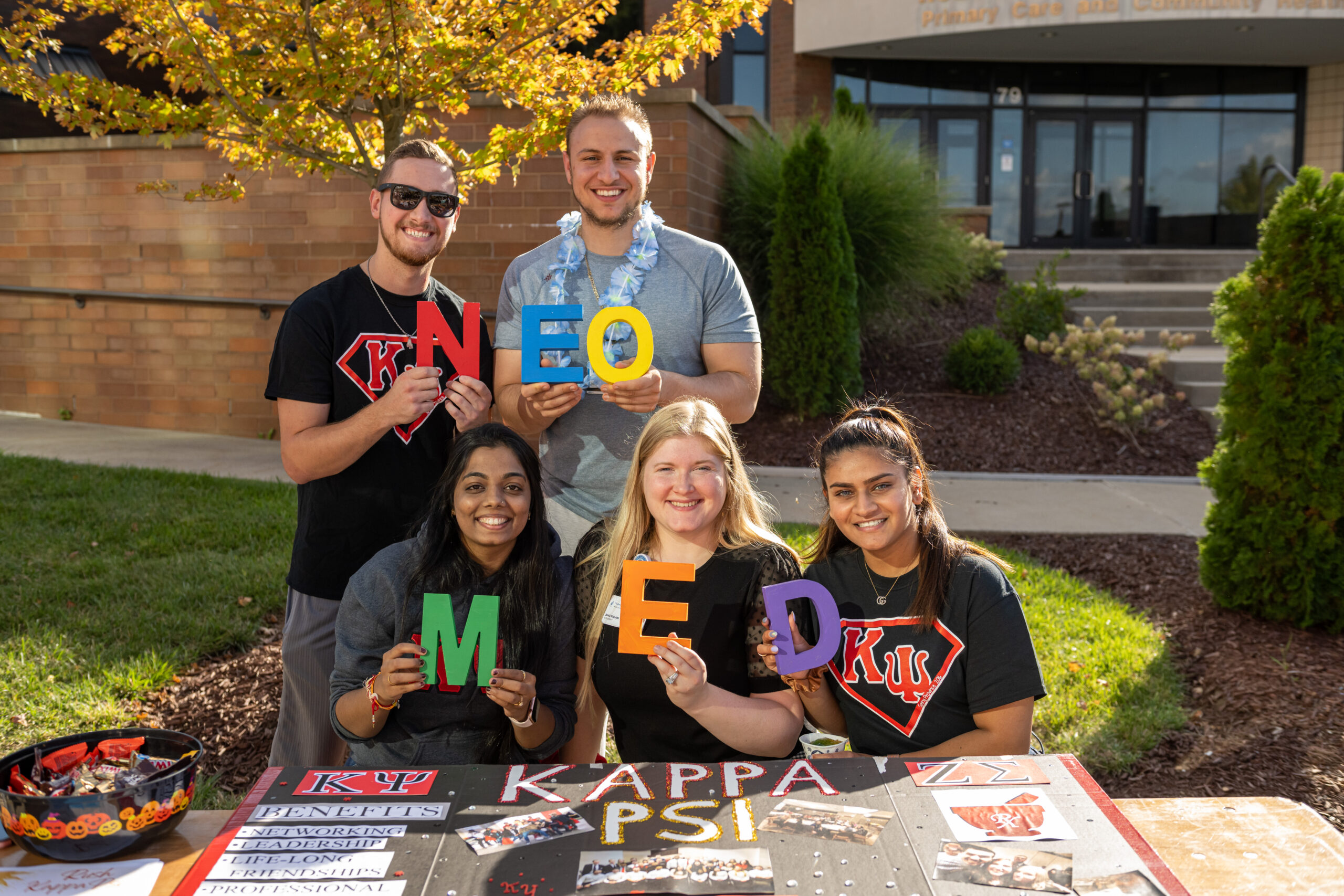 Students at a table hold letters that spell the word NEOMED.