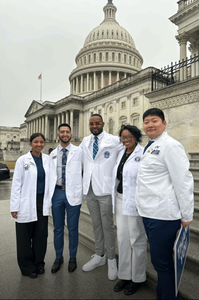 group of pharmacy students in white coats pose in front of the Capitol dome