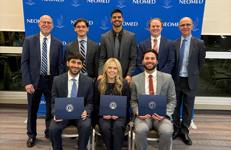 AOA officers and inductees pose in front of a NEOMED backdrop