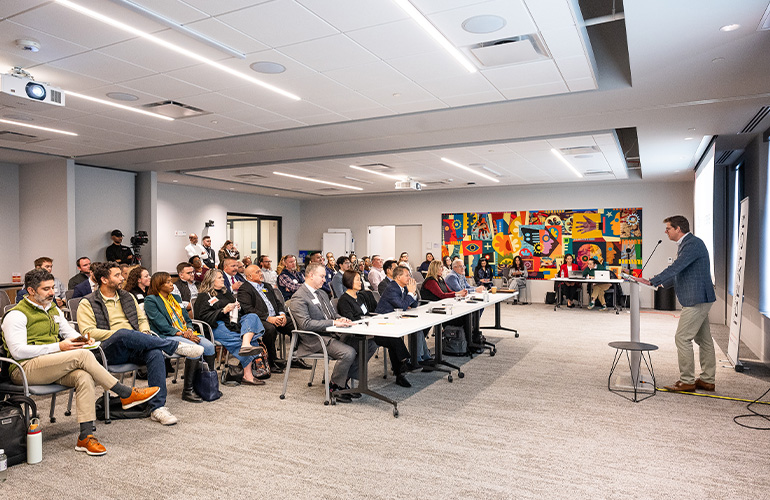 A man at a podium addresses a group of people in a classroom