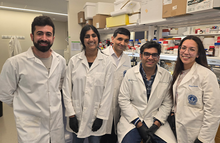 Five people in white coats pose in a science lab