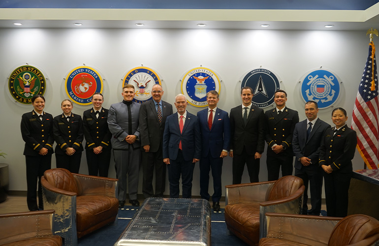a group of people, most wearing military uniforms, post in front of seals from service branches