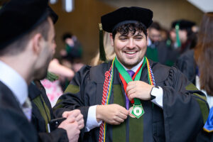 a young man with a beard is dressed in academic regalia for the Pharm.D. degree
