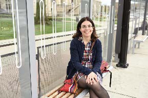 snapshot of casually dressed young woman with glasses sitting on a bench outside