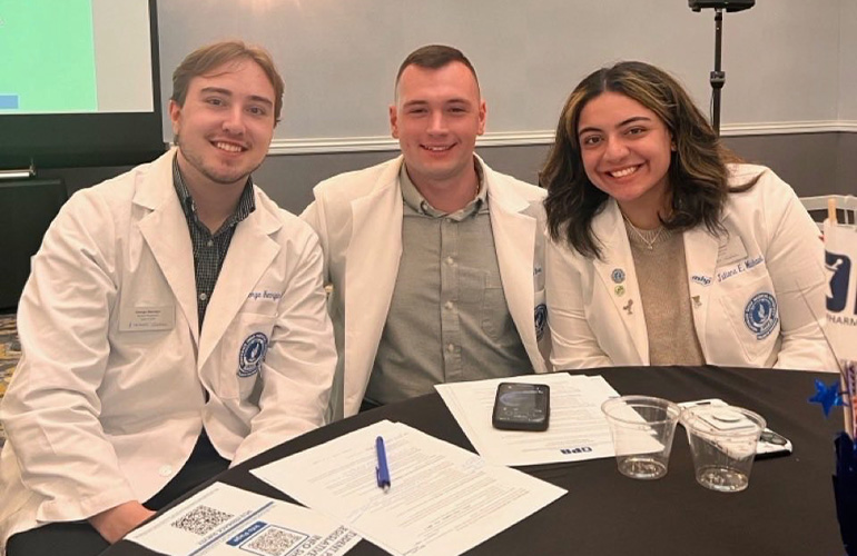 three pharmacy students in white coats smile at the camera