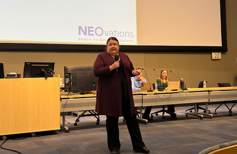 Woman in maroon jacket presents in front of a lecture hall