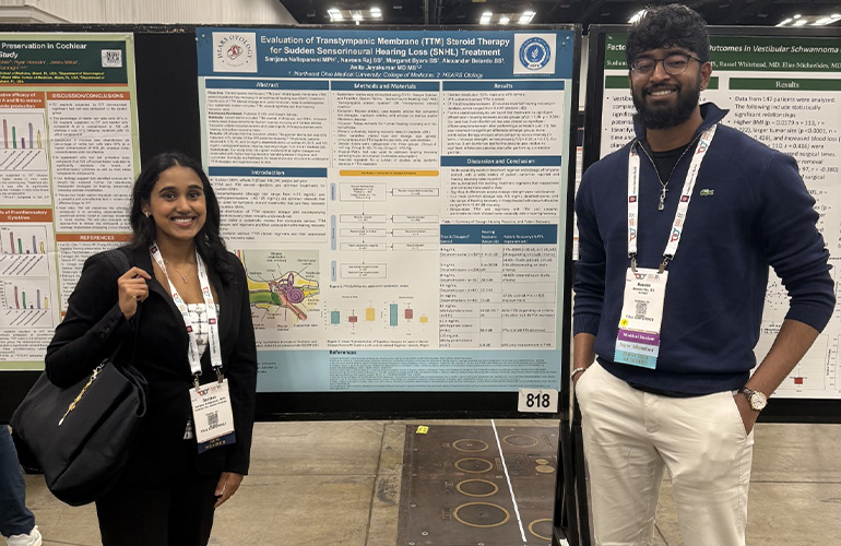 Young woman and young man stand in front of an academic poster at a conference