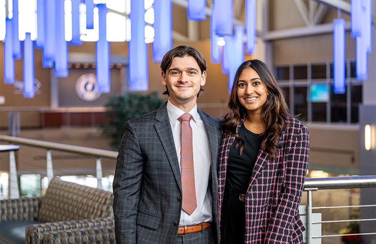 Two young people in business casual attire smile at the camera