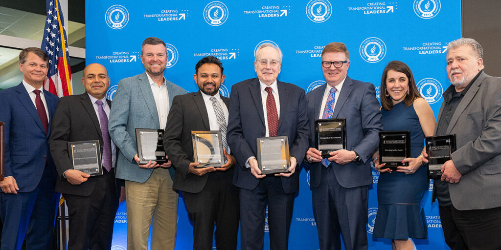 group of people dressed in business attire pose with award plaques in front of a NEOMED step-and-repeat backdrop