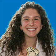 A student in a white coat holding a cookie and smiling.