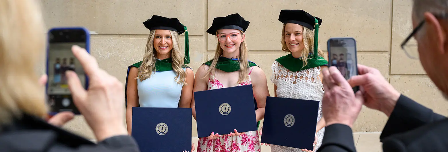 Three students in their commencement robes stand for a picture.