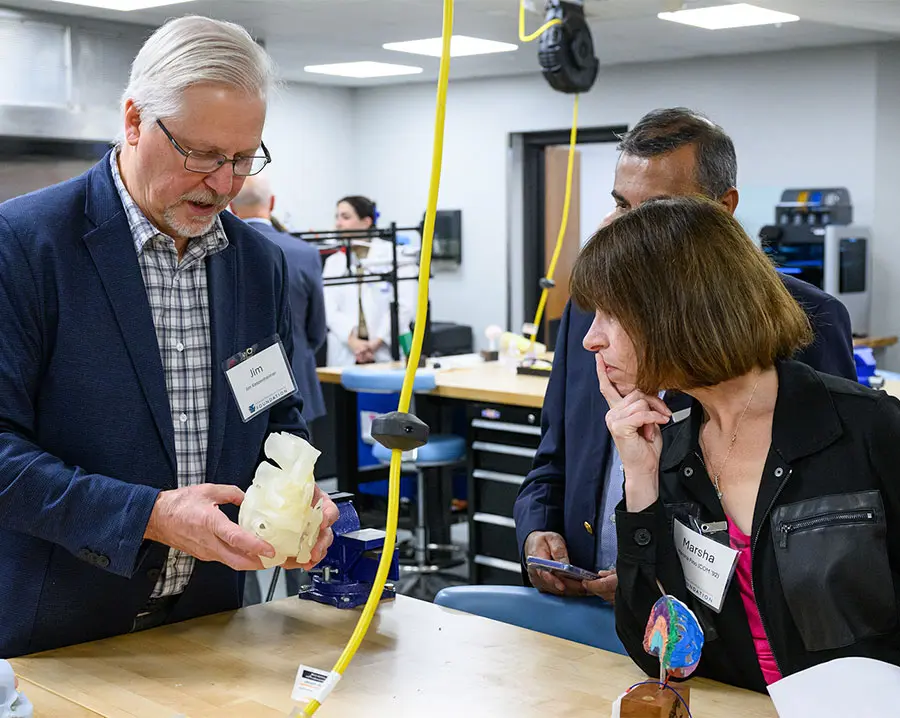 Three people in a lab examine anatomical models and equipment during a health education demonstration.