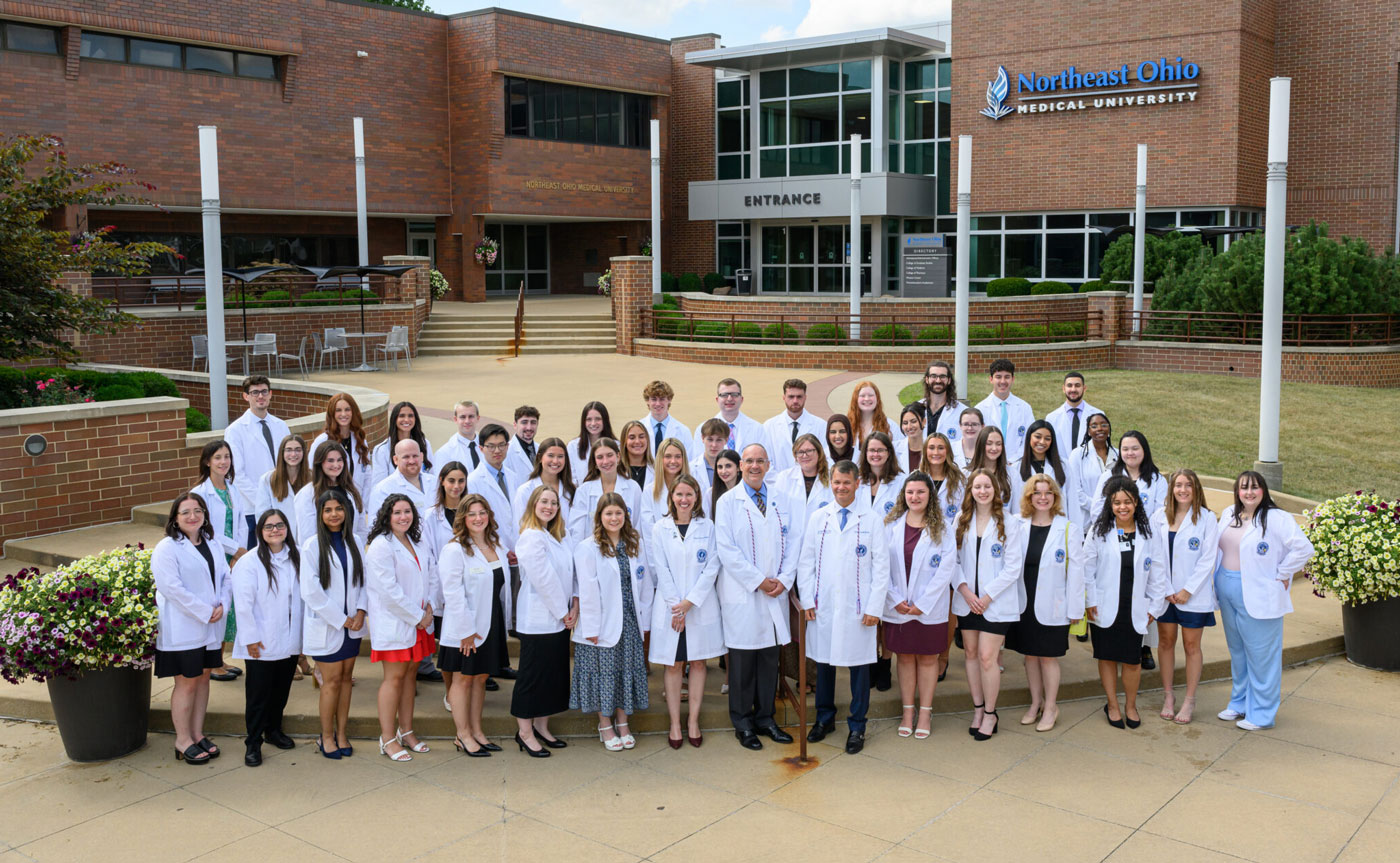 Pharmacy students in their white coats stand outside of NEOMED's main entrance.