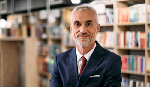 A professor with his arms crossed in front of a bookcase.