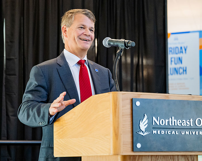 A speaker in a coat and tie gestures at a podium.