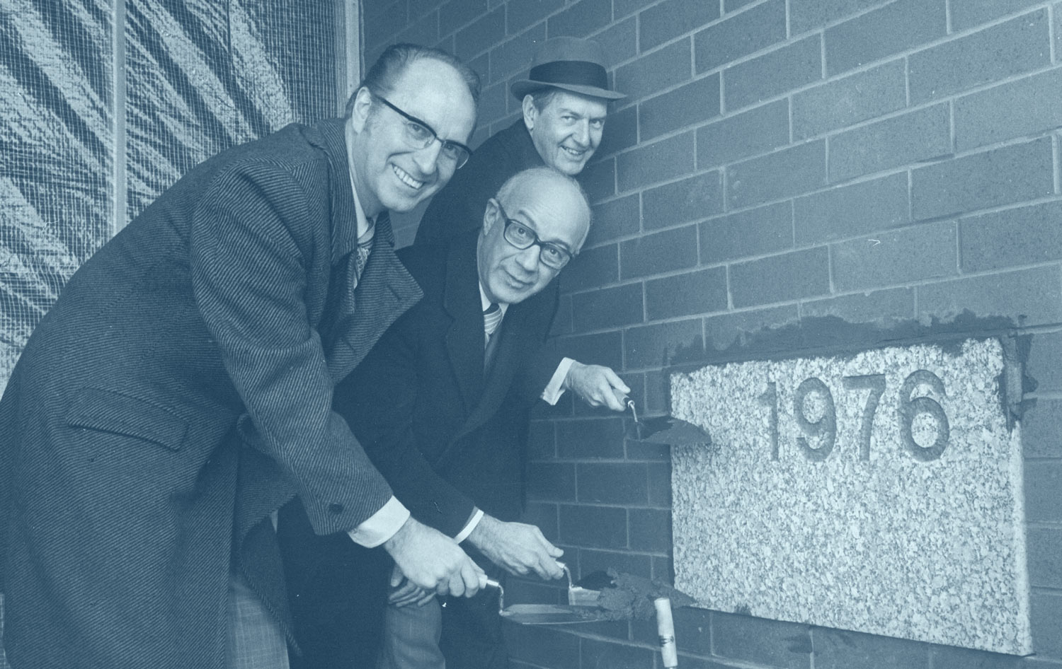 Three men in coats and ties add mortar to a cornerstone at NEOMED.