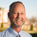 A man in a coat and tie on a sunny day on campus.
