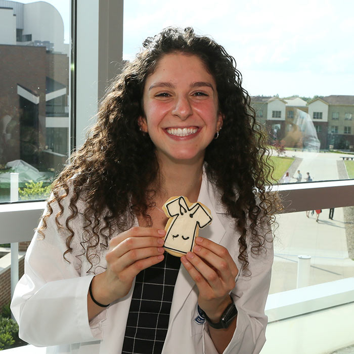 A student in a white coat holds up a cookie that looks like a white coat.