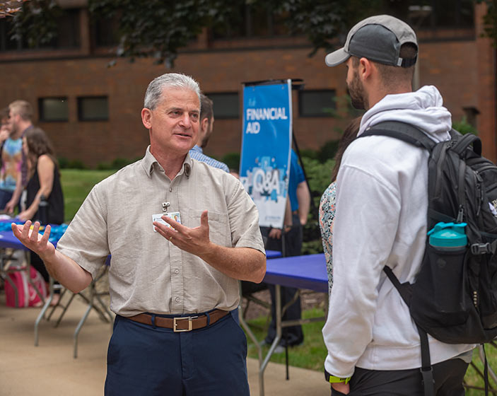 A man in a collared shirt talks with a student outdoors at NEOMED.